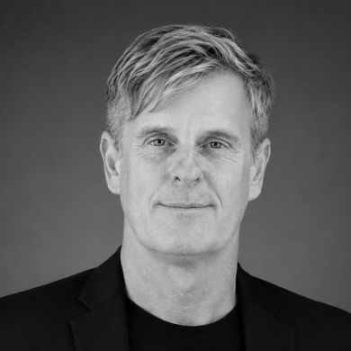 Smiling man in a dark blazer against a plain gray background