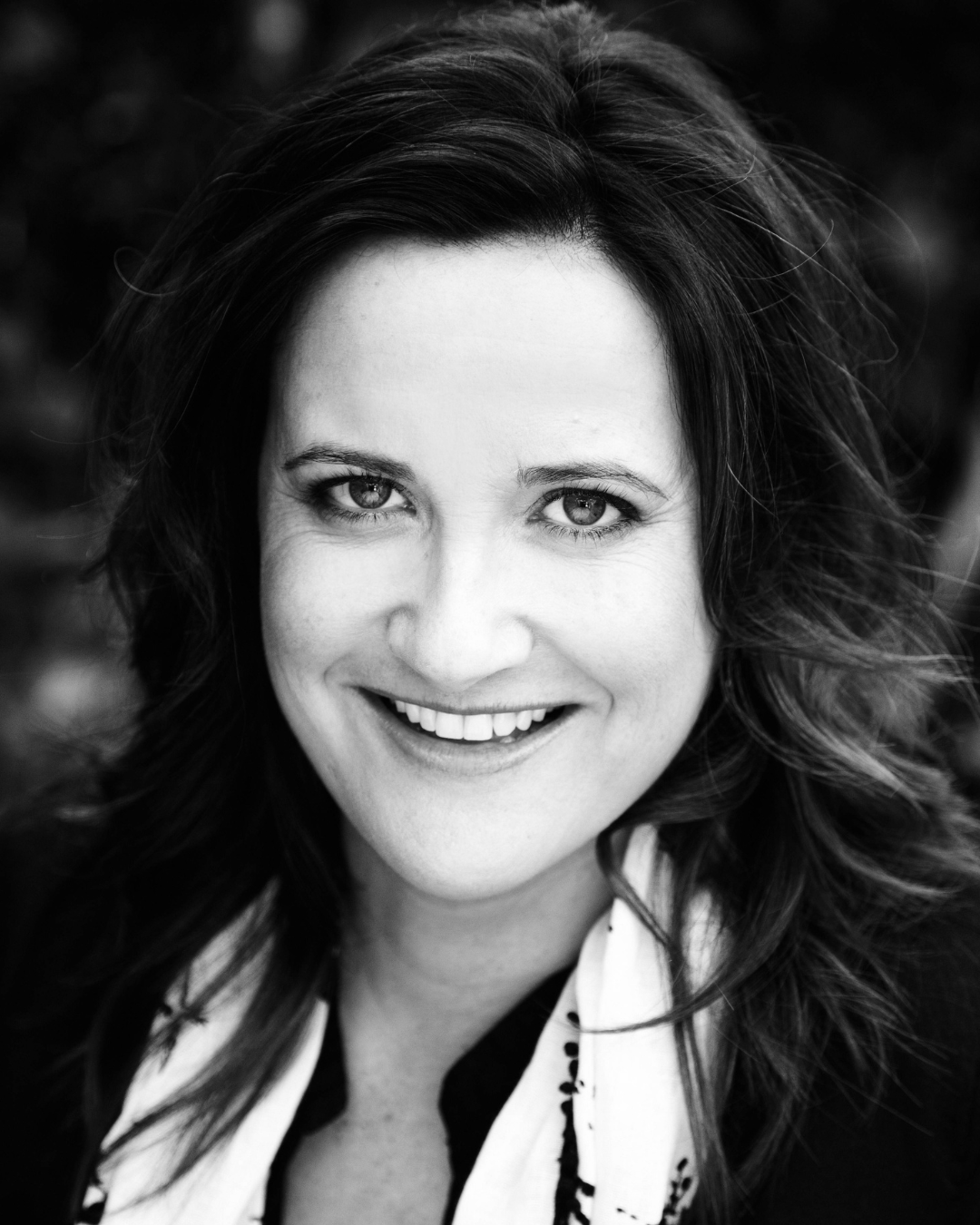 Black-and-white close-up portrait of a smiling person with wavy hair, facing the camera.