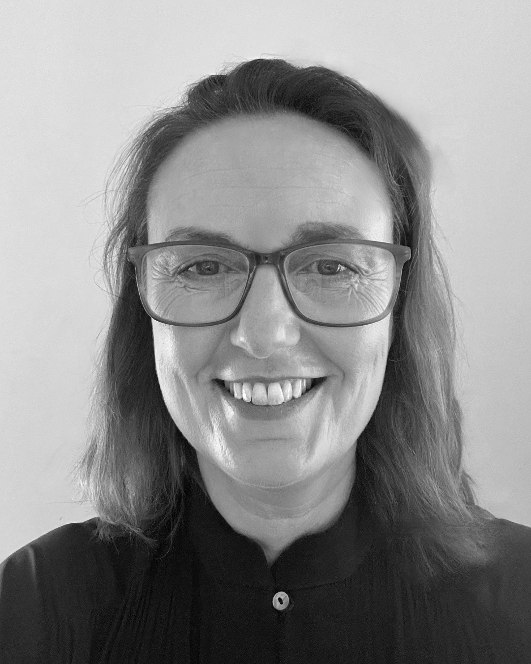 Portrait of a smiling person wearing glasses and a dark top, against a plain background