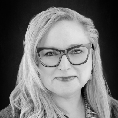 Black-and-white portrait of a woman with long blonde hair and large glasses, facing the camera.
