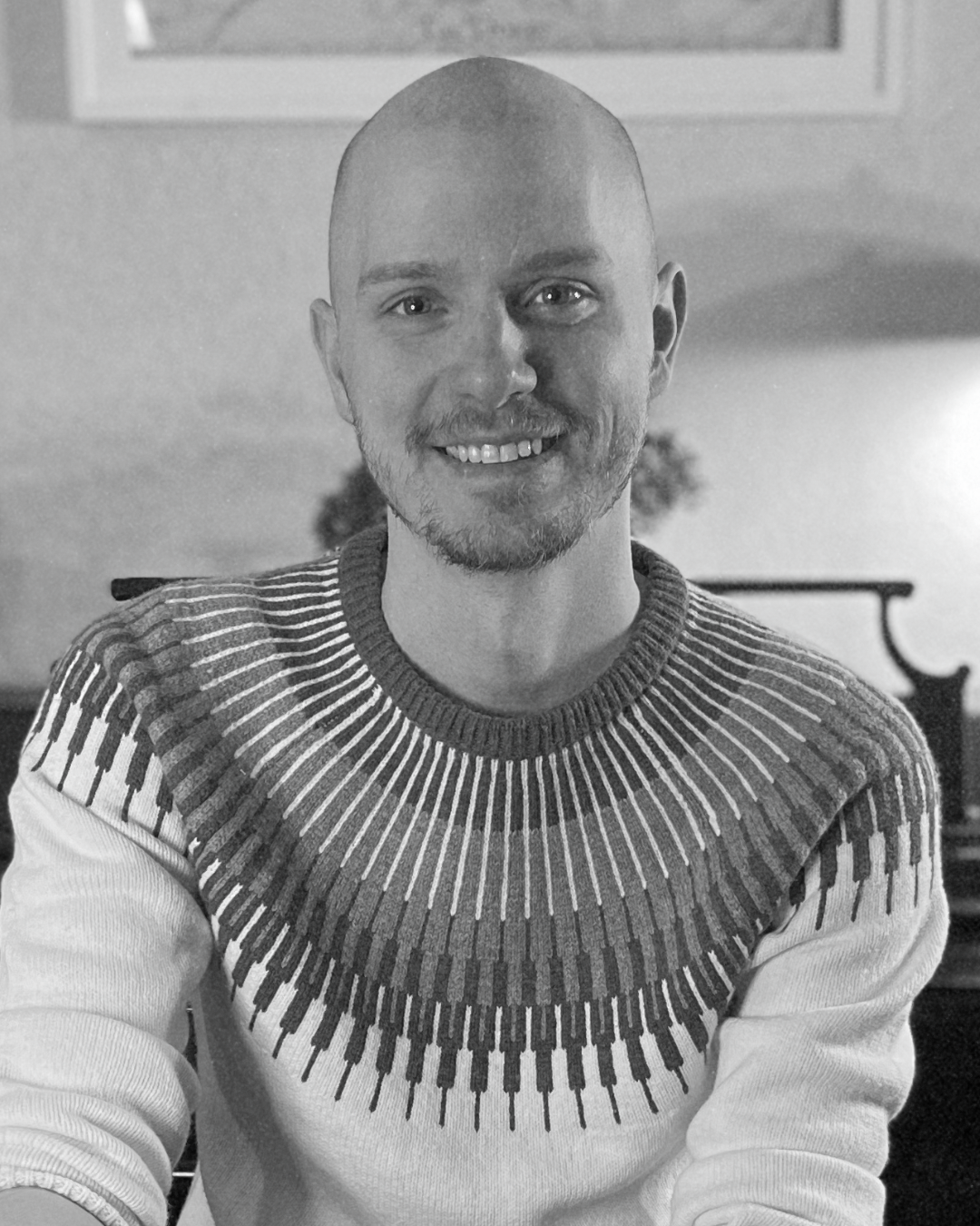 Smiling bald man in patterned sweater sitting indoors in a living room