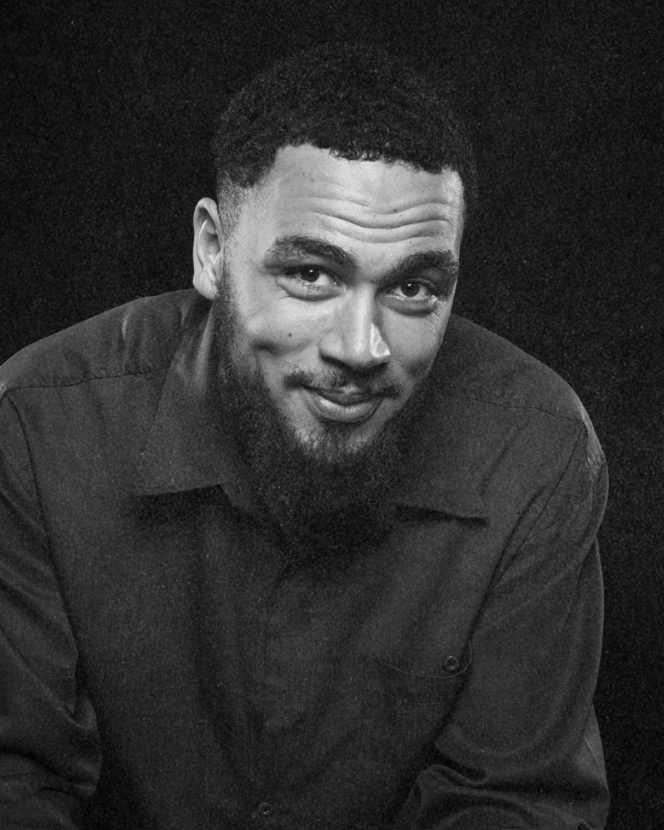 Black-and-white portrait of a smiling man leaning slightly forward in a dark shirt.