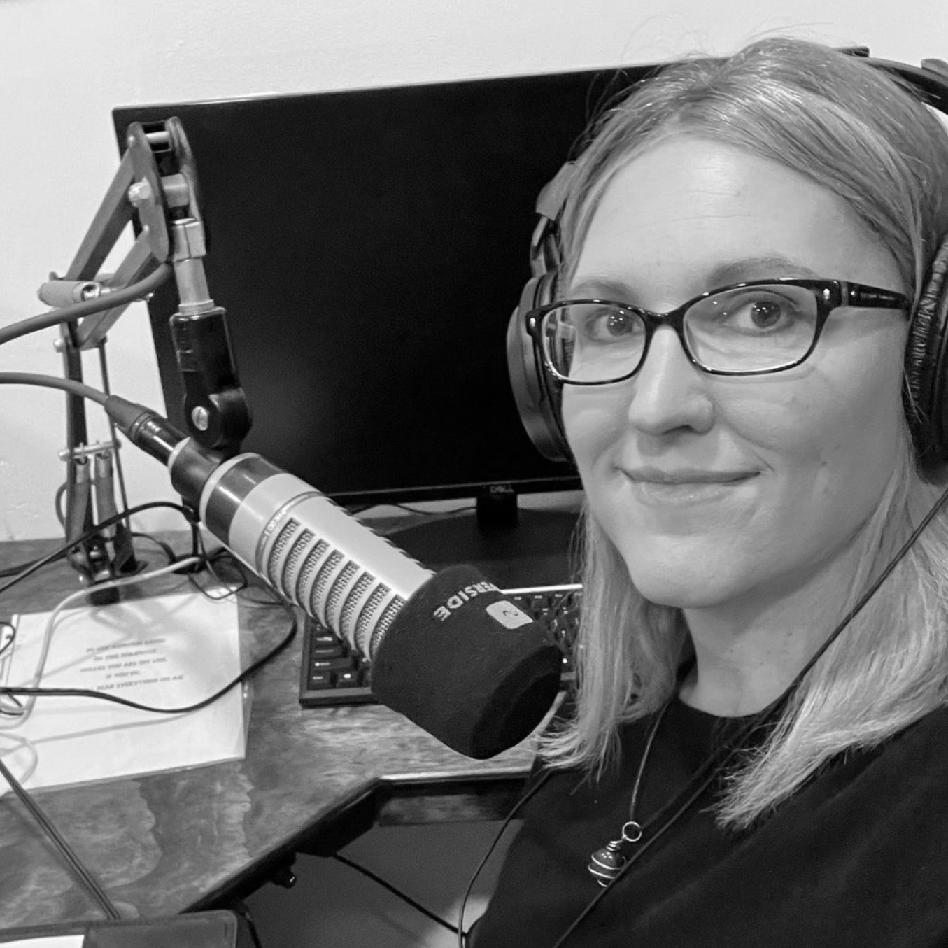 Woman wearing headphones beside a microphone in a podcast studio, smiling at the camera.