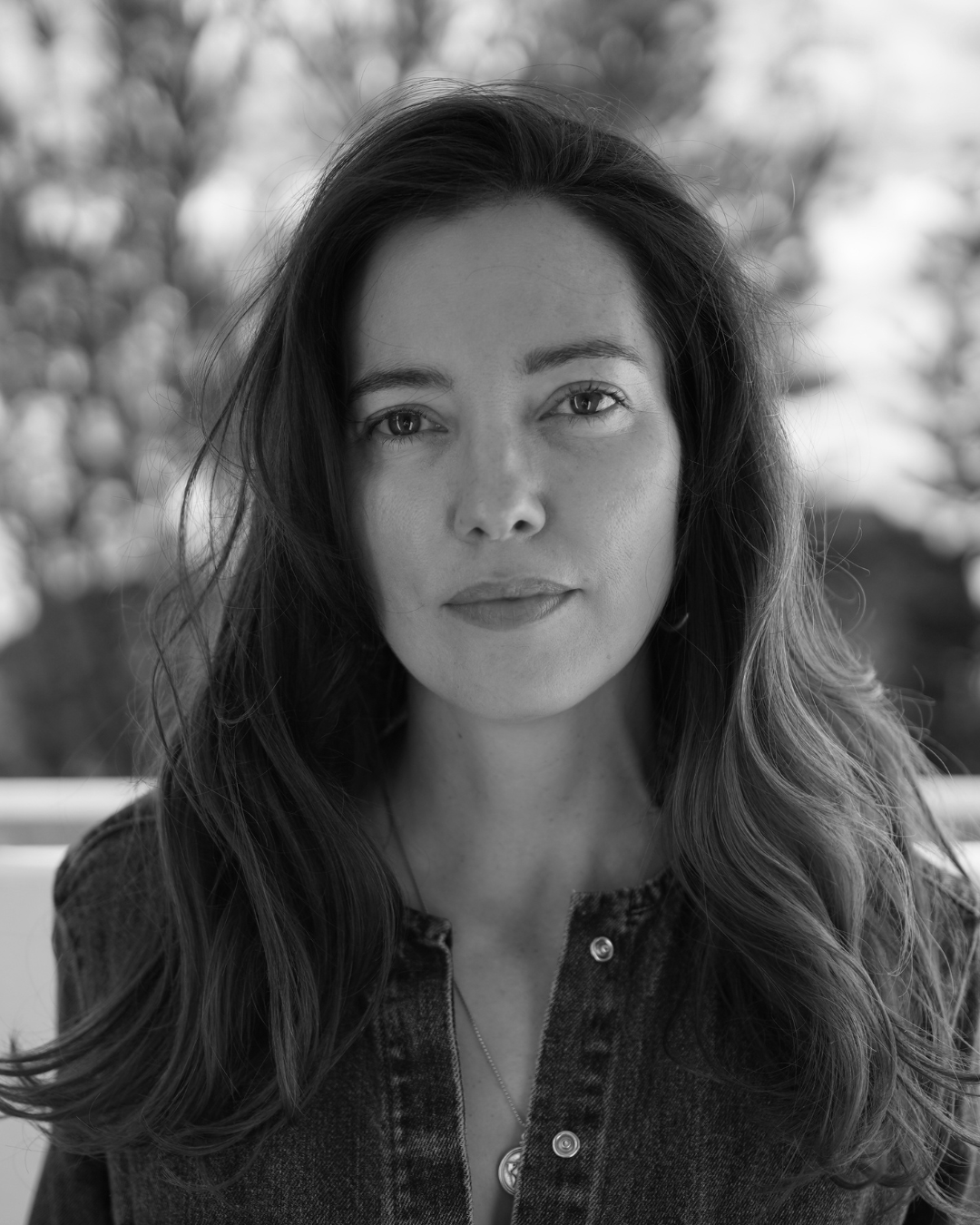 Black-and-white portrait of a woman with long hair, looking directly at the camera outdoors