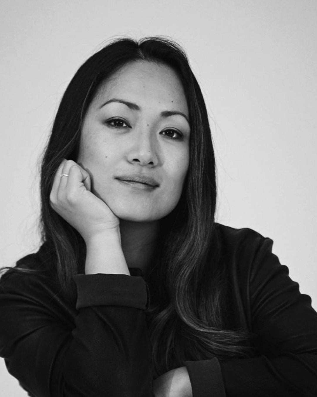 Black-and-white portrait of a person resting their chin on their hand, looking at the camera.