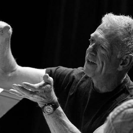 Black-and-white portrait of a smiling person gesturing with raised hands against a dark background