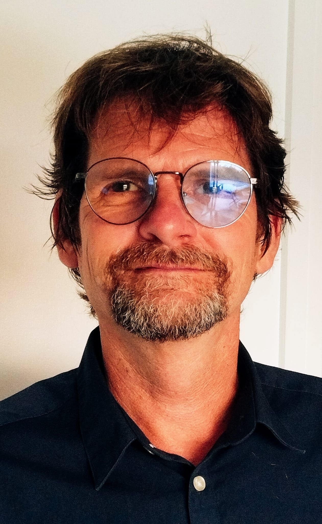 Man with glasses and beard, wearing a dark shirt, looking at the camera.