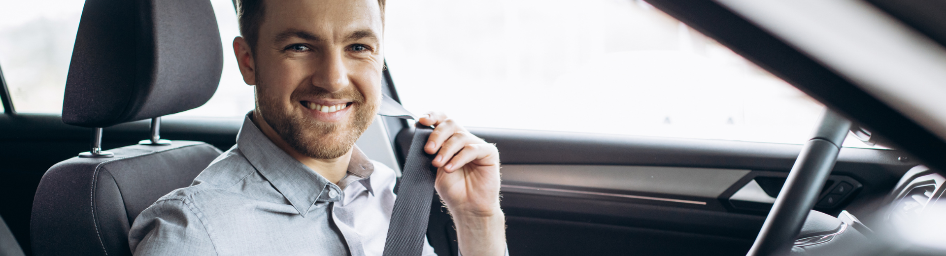 Motorista sorridente, usando cinto de segurança e segurando um telefone no interior de um carro.