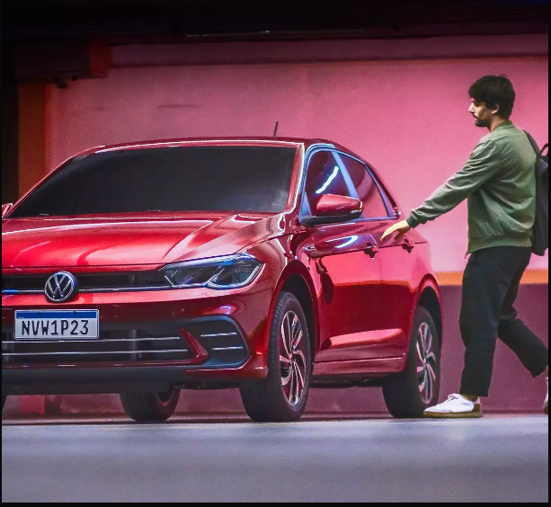 Homem empurrando um Volkswagen Sedan vermelho em frente a uma parede rosa.