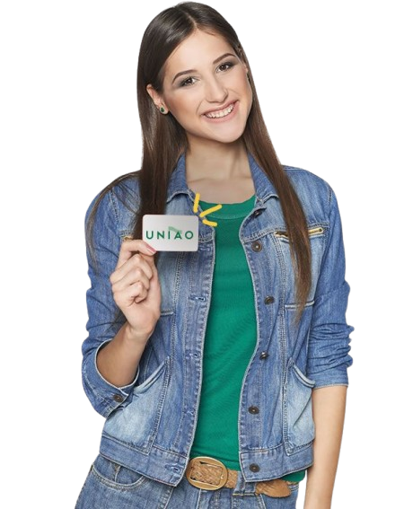 Mulher sorrindo, segurando um cartão com letras verdes, vestindo uma jaqueta jeans e uma camisa verde.