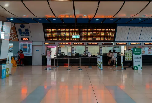 Balcões de venda de bilhetes em uma estação de trem, com painéis de horários acima e um piso brilhante e refletivo.