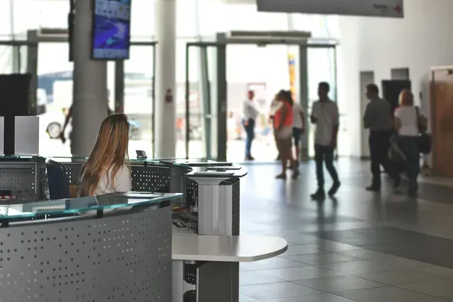 Mulher na recepção com pessoas entrando e saindo de um prédio.