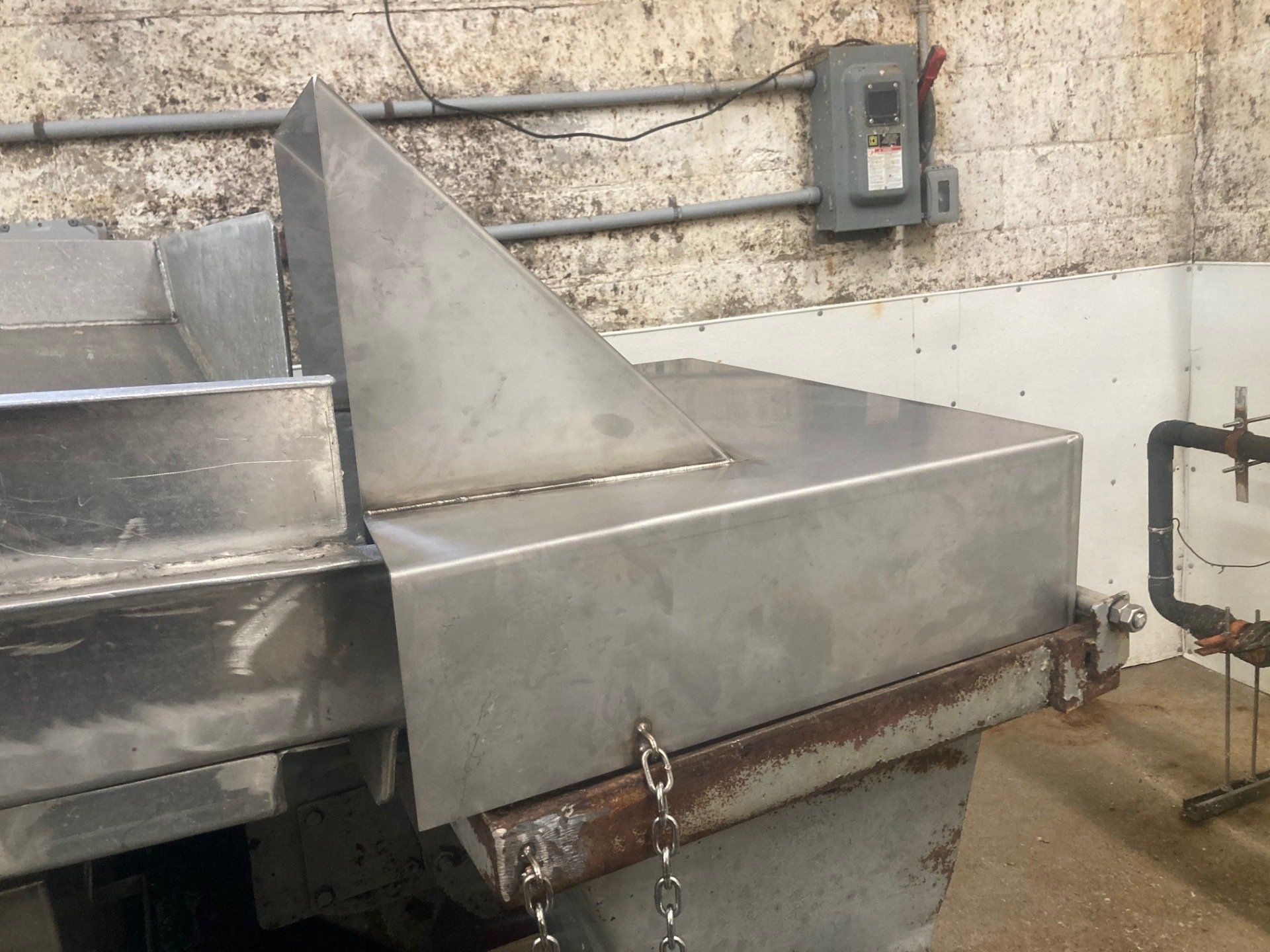 A stainless steel machine is sitting in a room next to a brick wall.