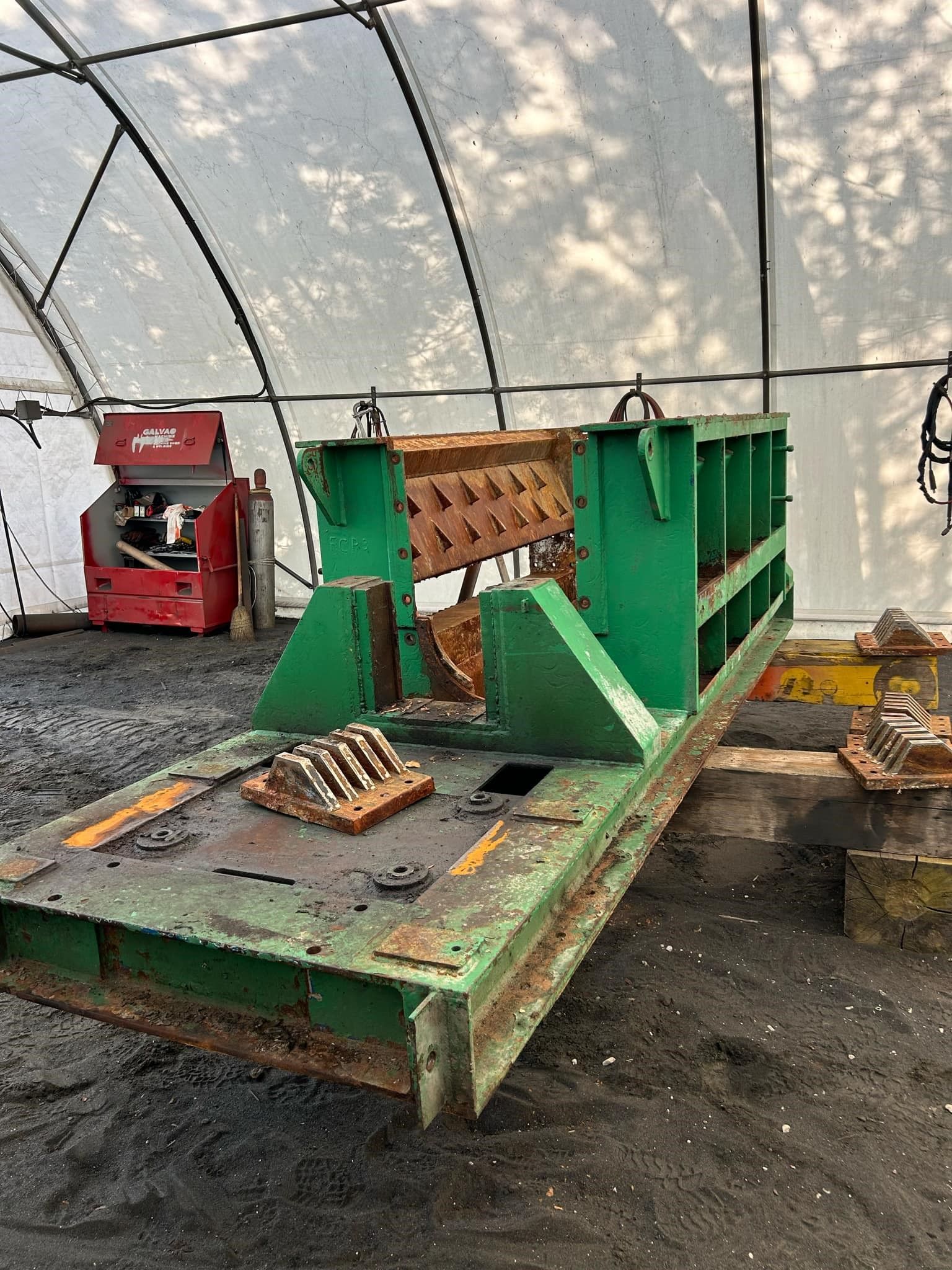 A green machine is sitting under a tent in a garage.