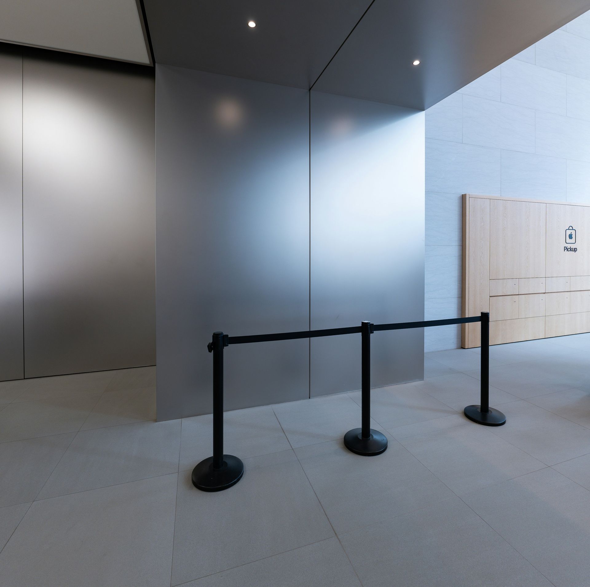 Modern building entrance with black queue stanchions and metal walls under bright skylights.