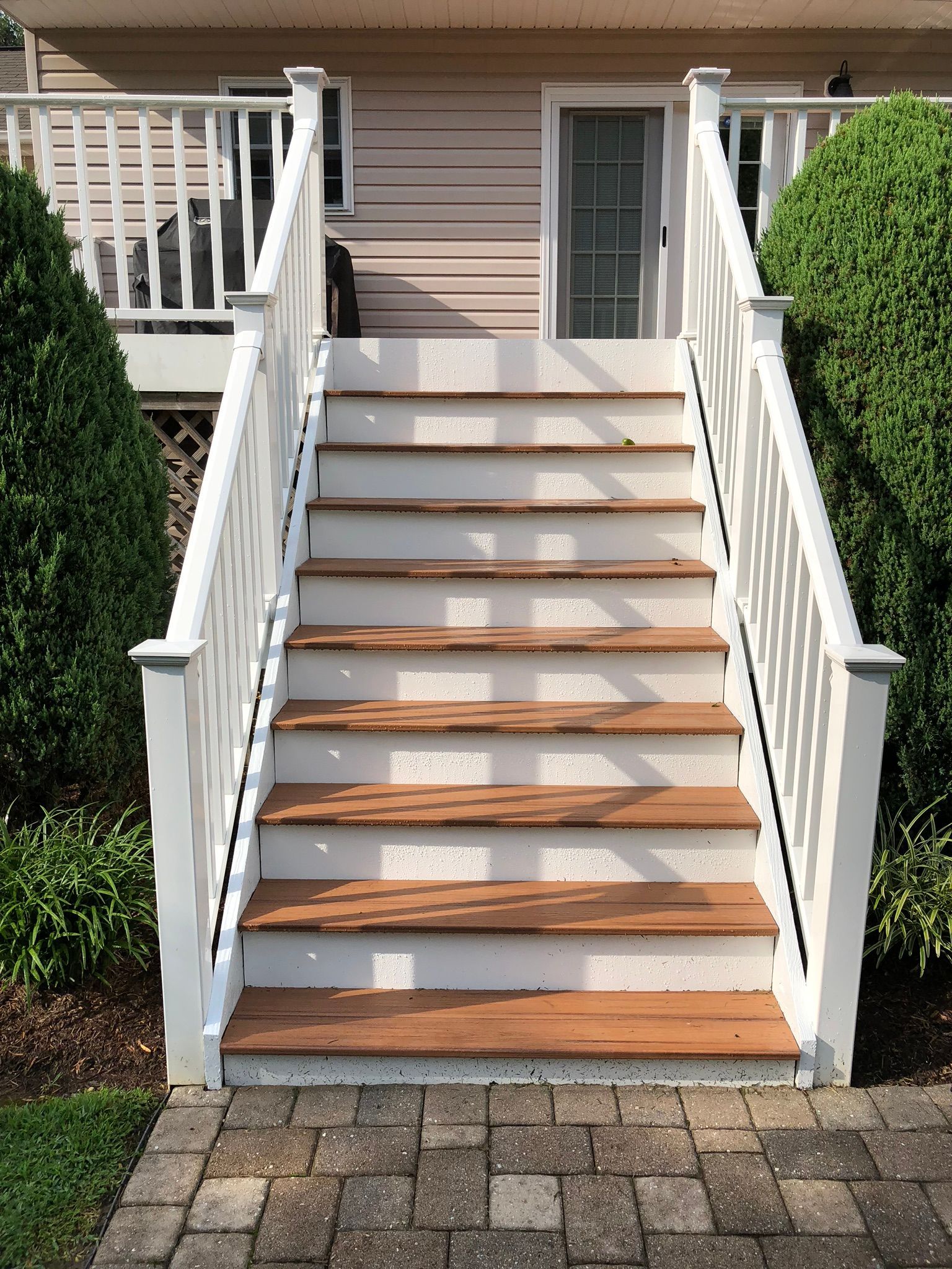 White wooden exterior staircase with railings leading to a house entrance, bordered by green shrubs.