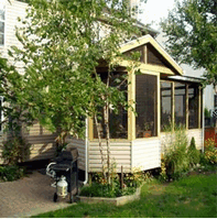 A house with a screened in porch and a grill in front of it