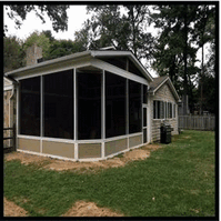 A screened in porch is sitting in the backyard of a house.