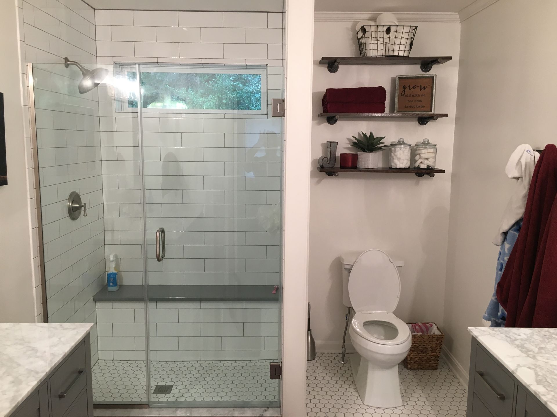 Bathroom with glass shower, white tile, and toilet beside wall shelves and towels