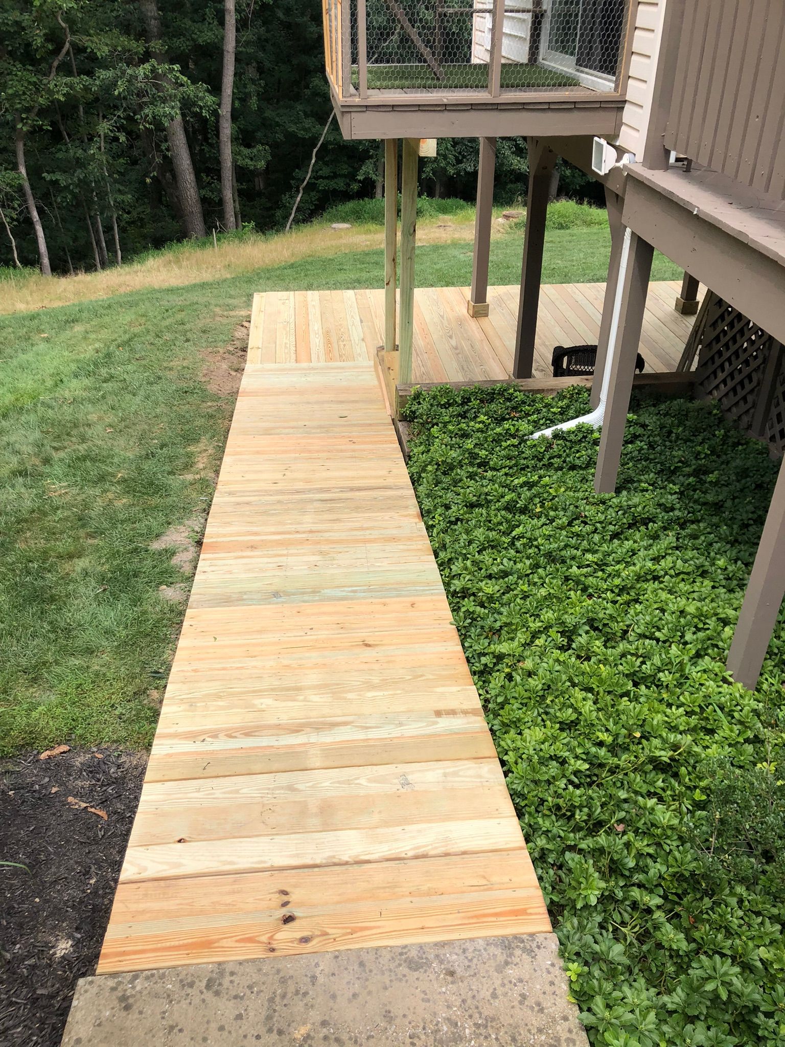 A wooden walkway leading to a deck in a backyard.