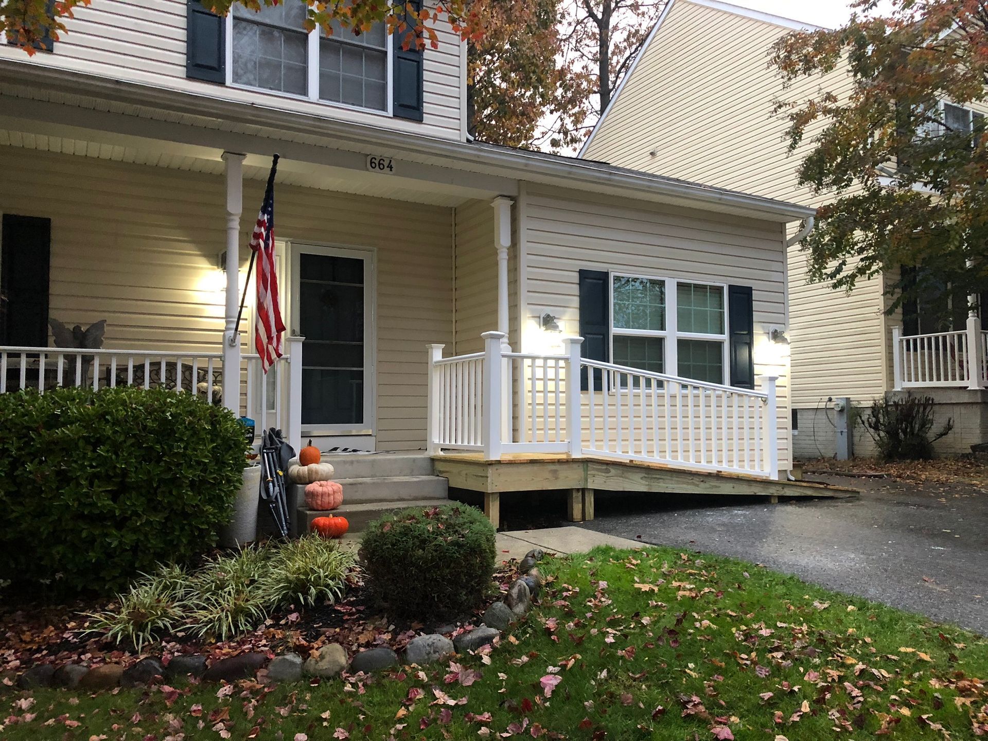 Suburban house porch with American flag, white railing, and autumn leaves on the lawn