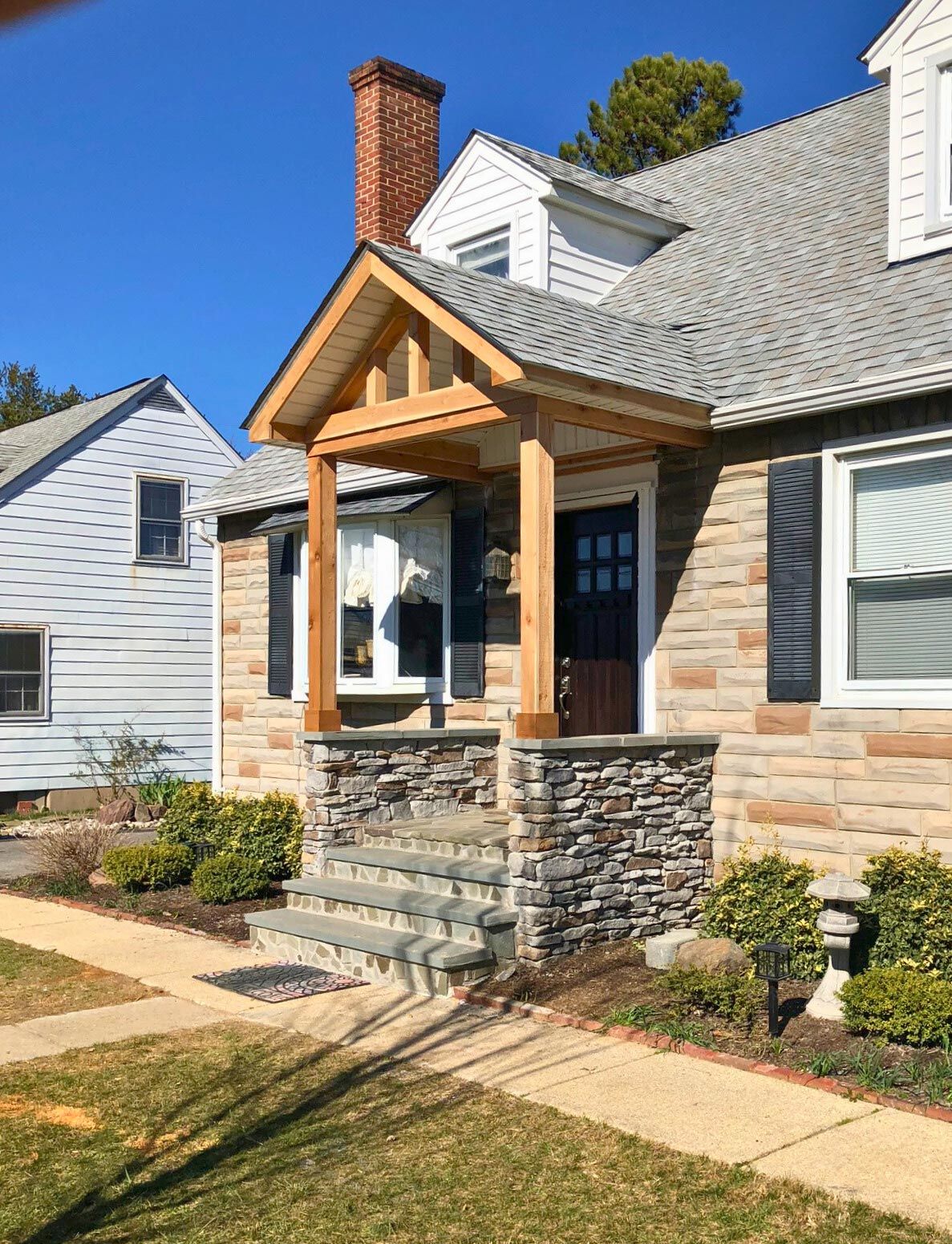 Stone-and-siding suburban house with a small front porch, blue front door, and manicured lawn