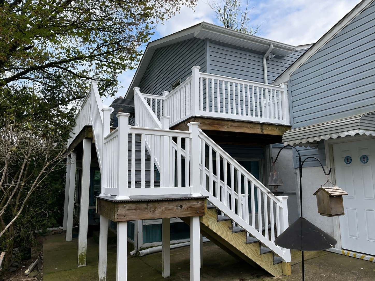 House exterior with raised deck, white stairs, and blue siding, viewed from the yard