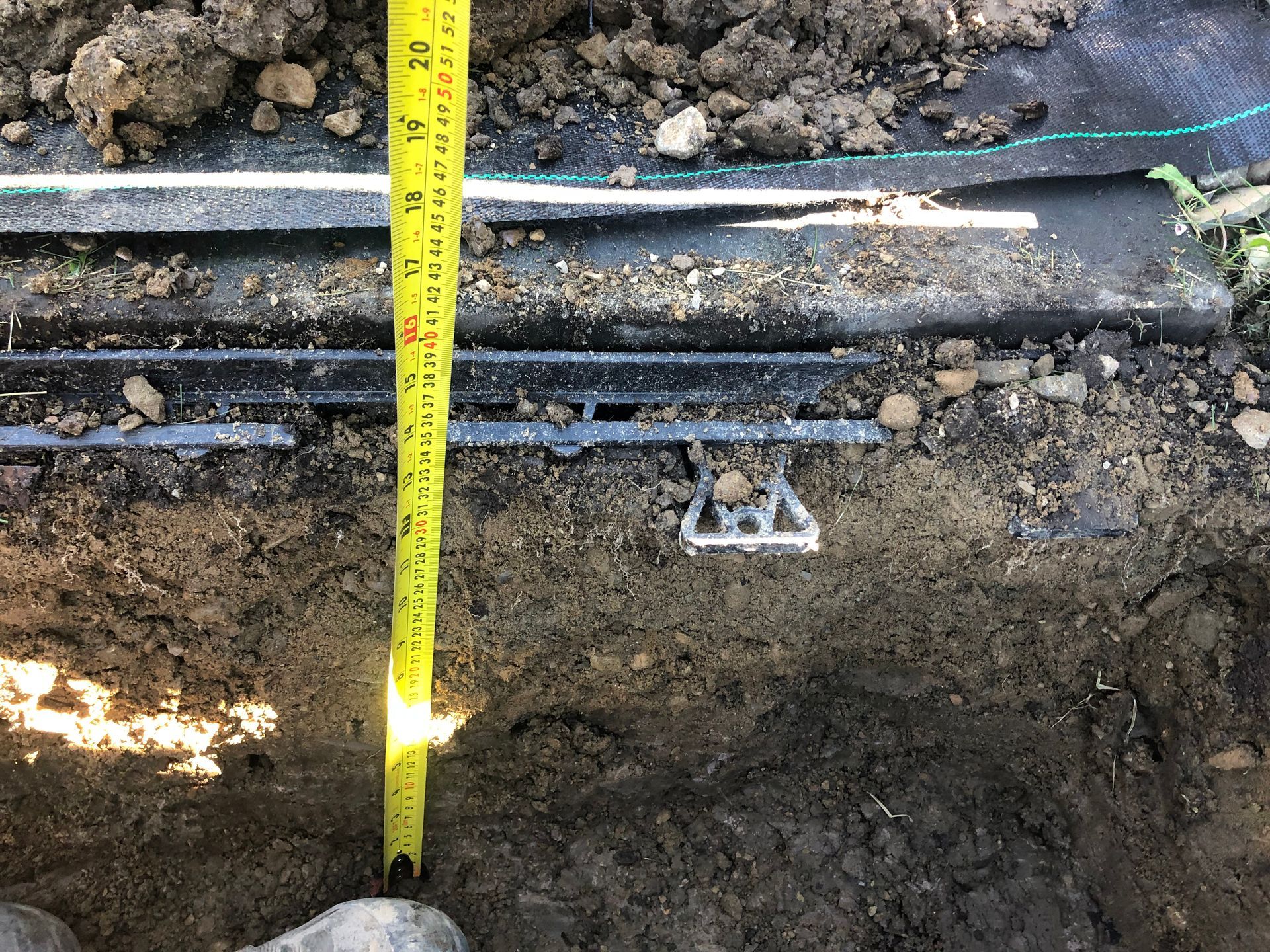A person is measuring the depth of a hole in the ground with a tape measure.