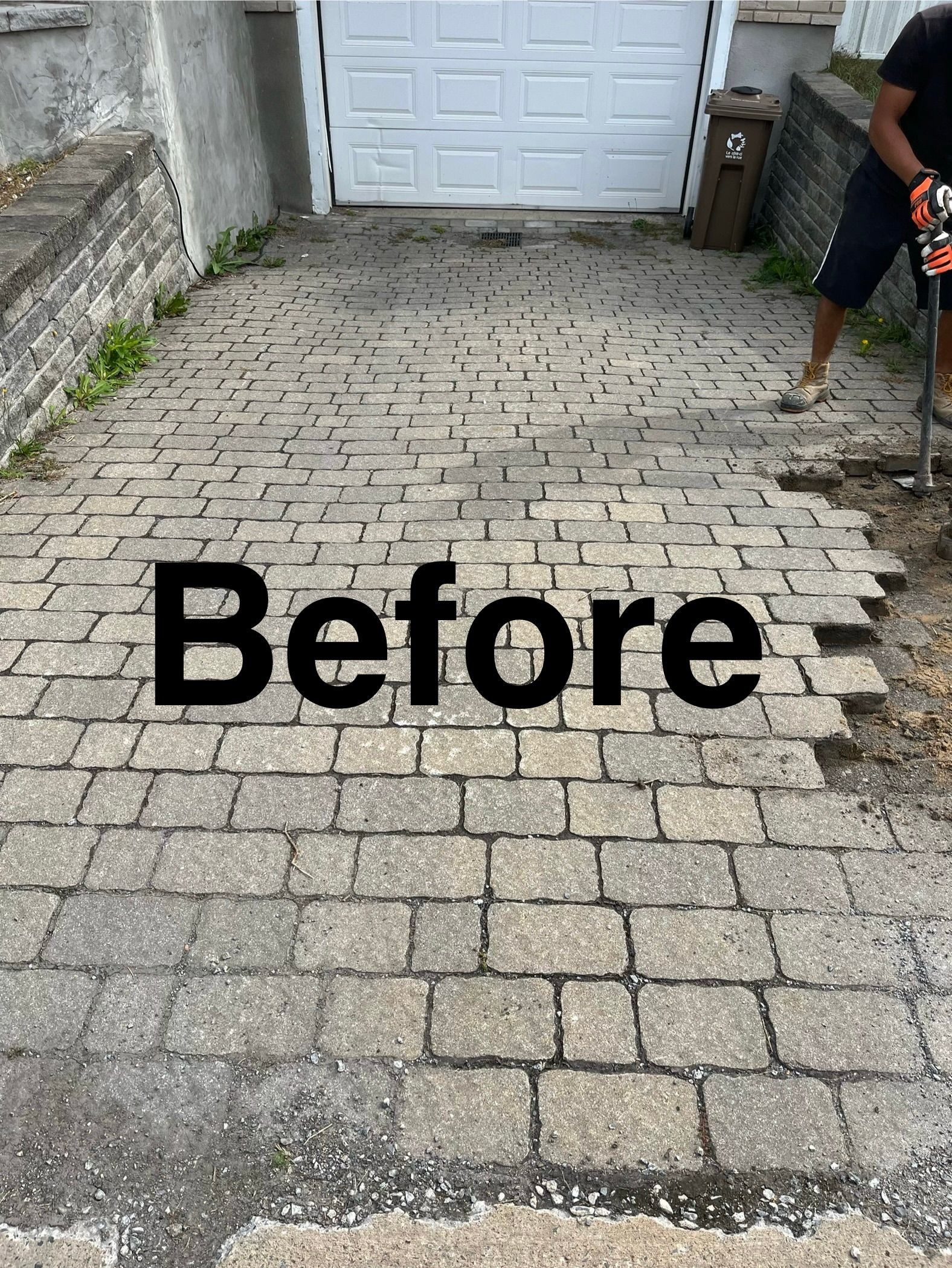 A man is working on a brick driveway in front of a garage.