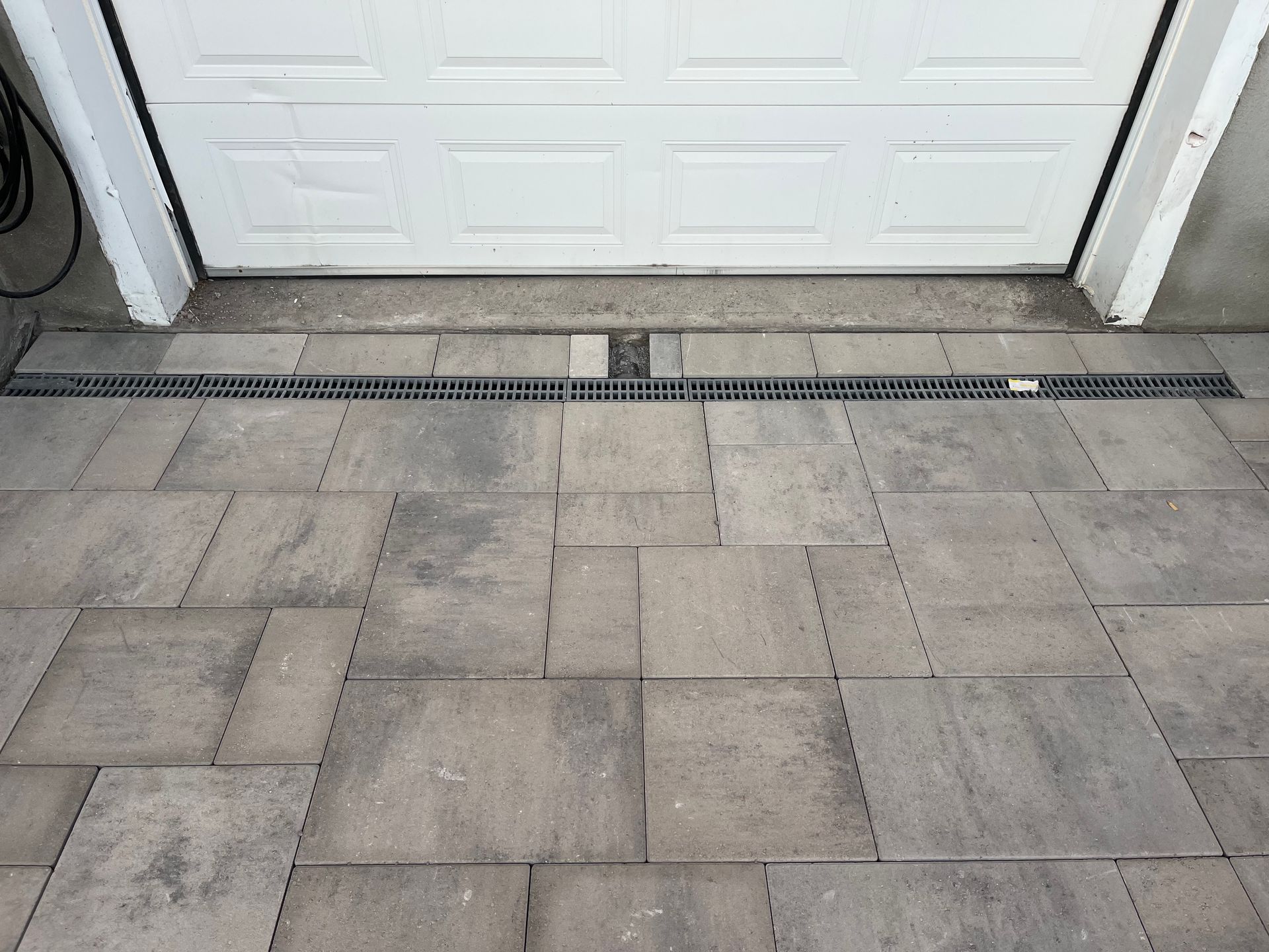 A driveway with a drain next to a garage door.