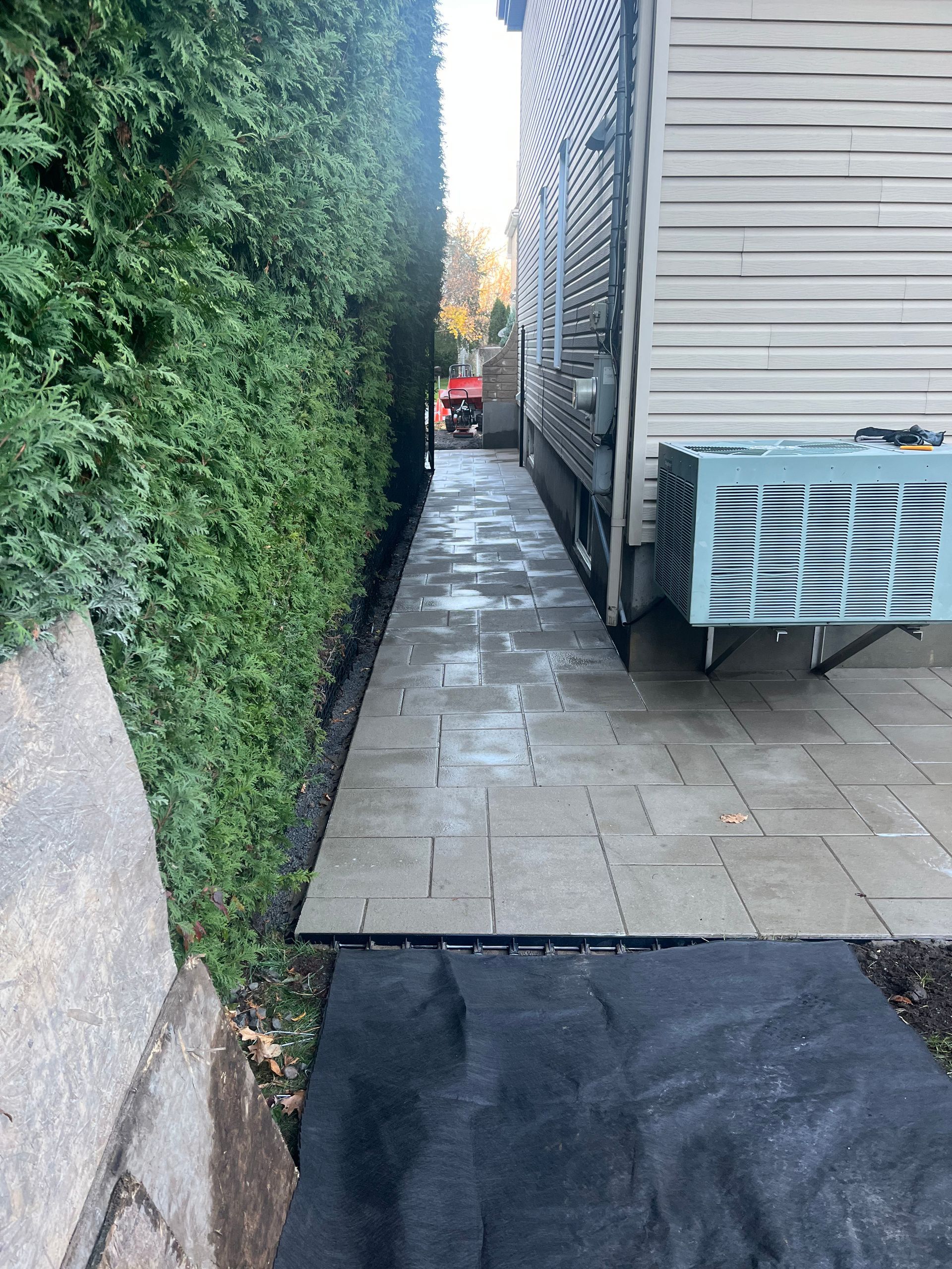A sidewalk leading to a house with an air conditioner on the side of it.