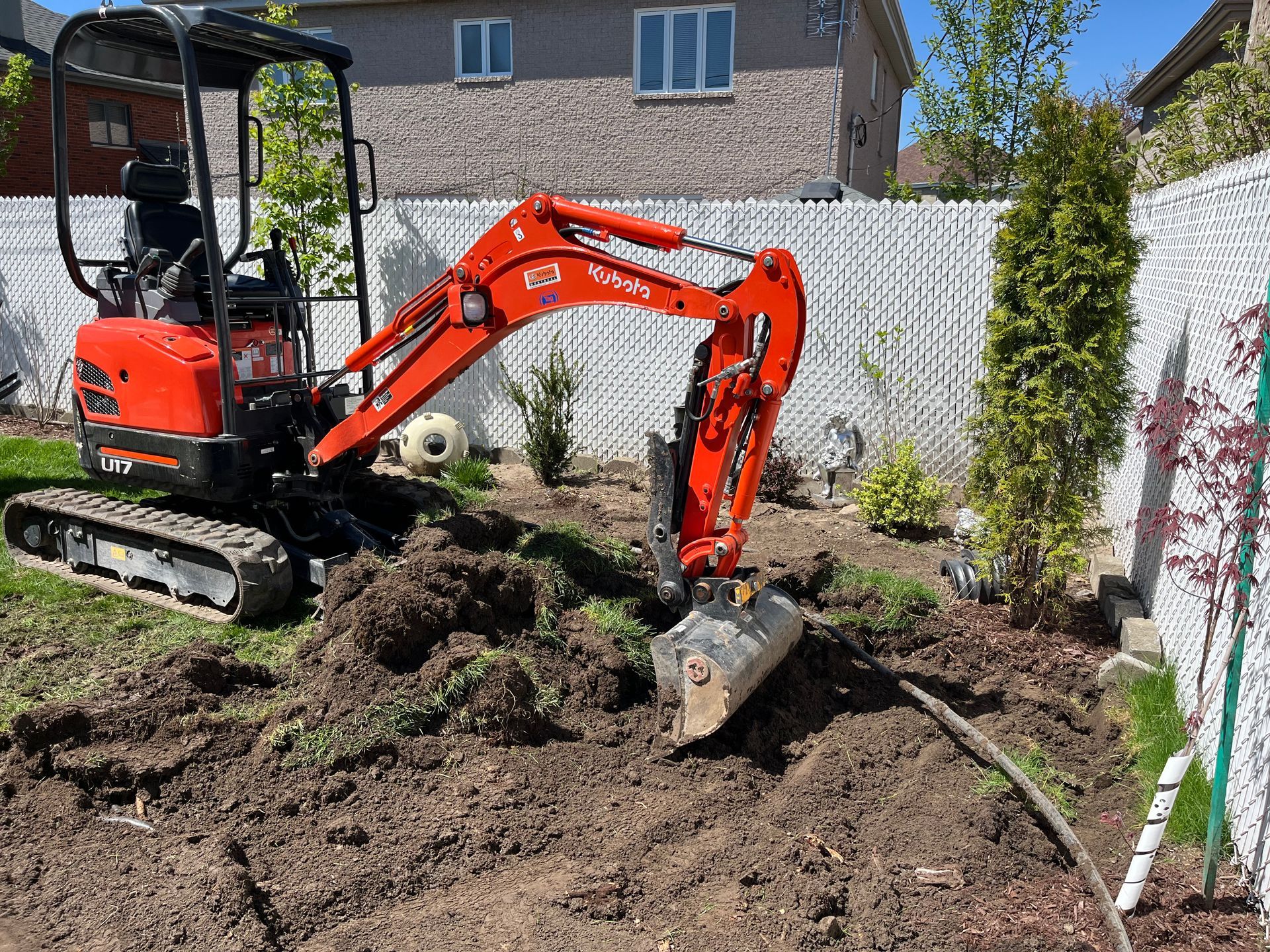 A small red excavator is digging a hole in a backyard.