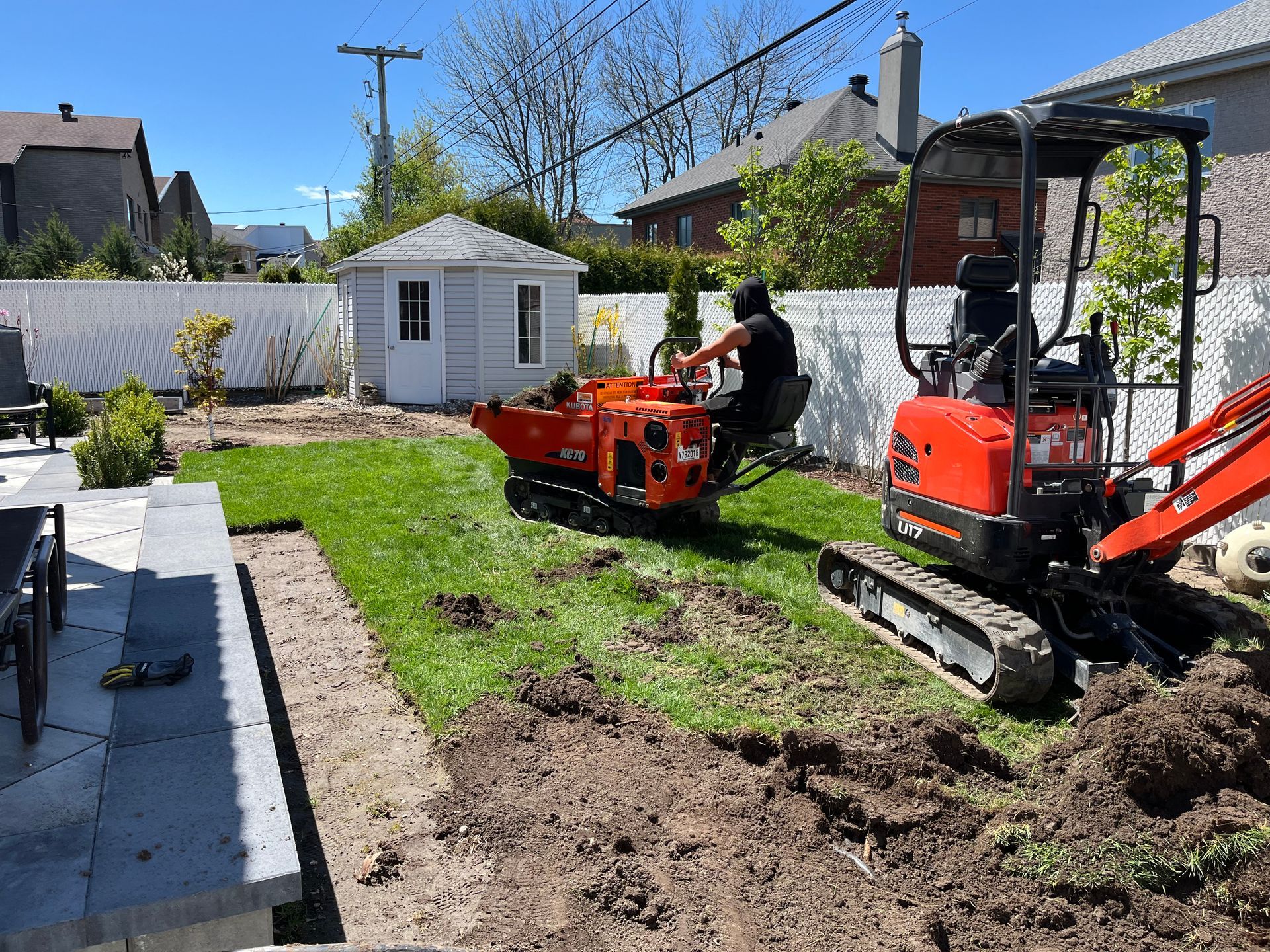 A man is driving a small excavator in a backyard.