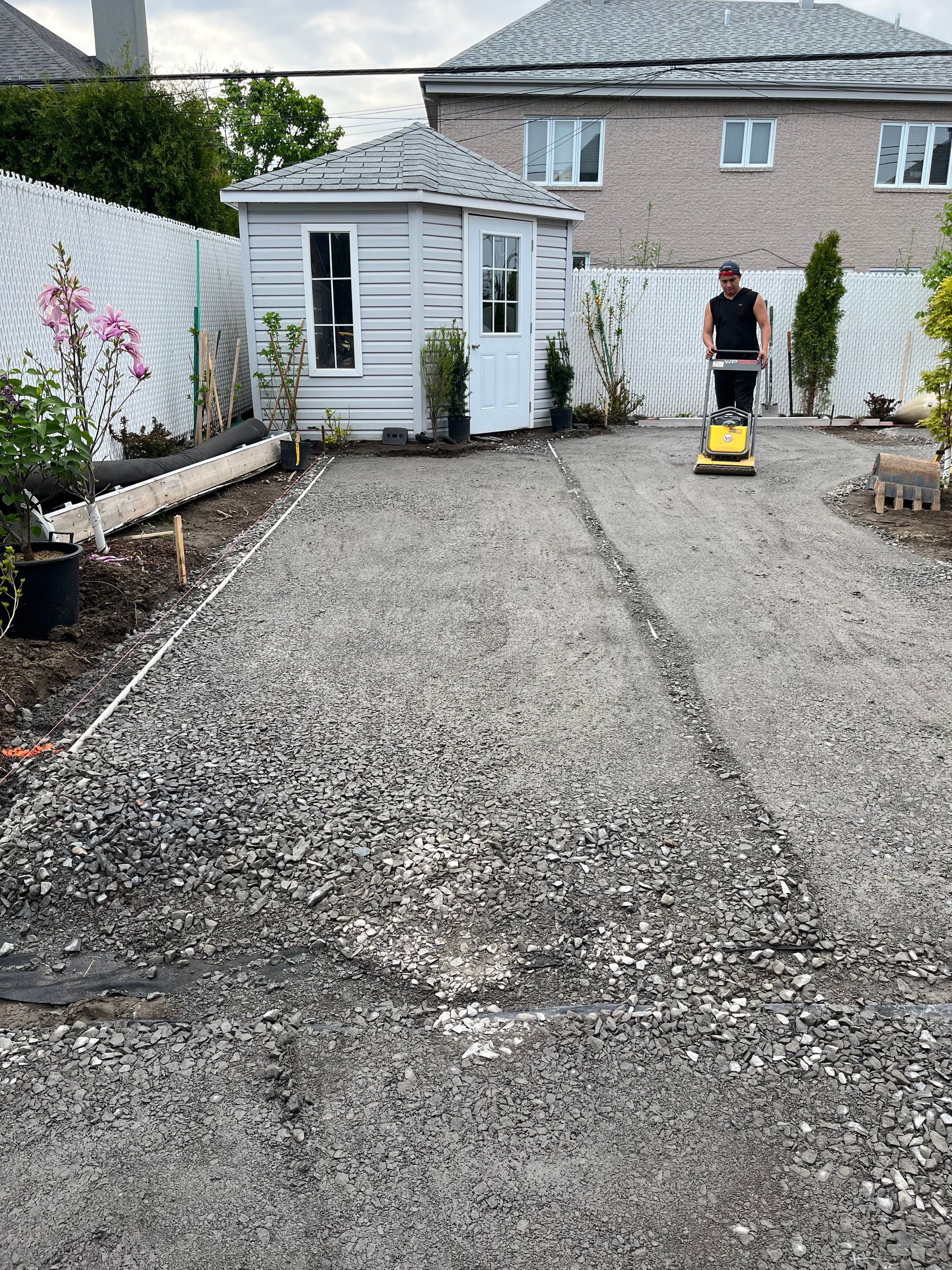 A man is using a vacuum cleaner to clean a gravel driveway in front of a house.