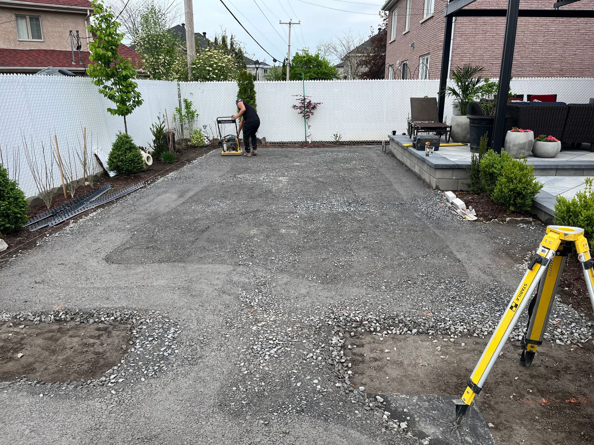 A person is standing in a gravel driveway next to a yellow tripod.