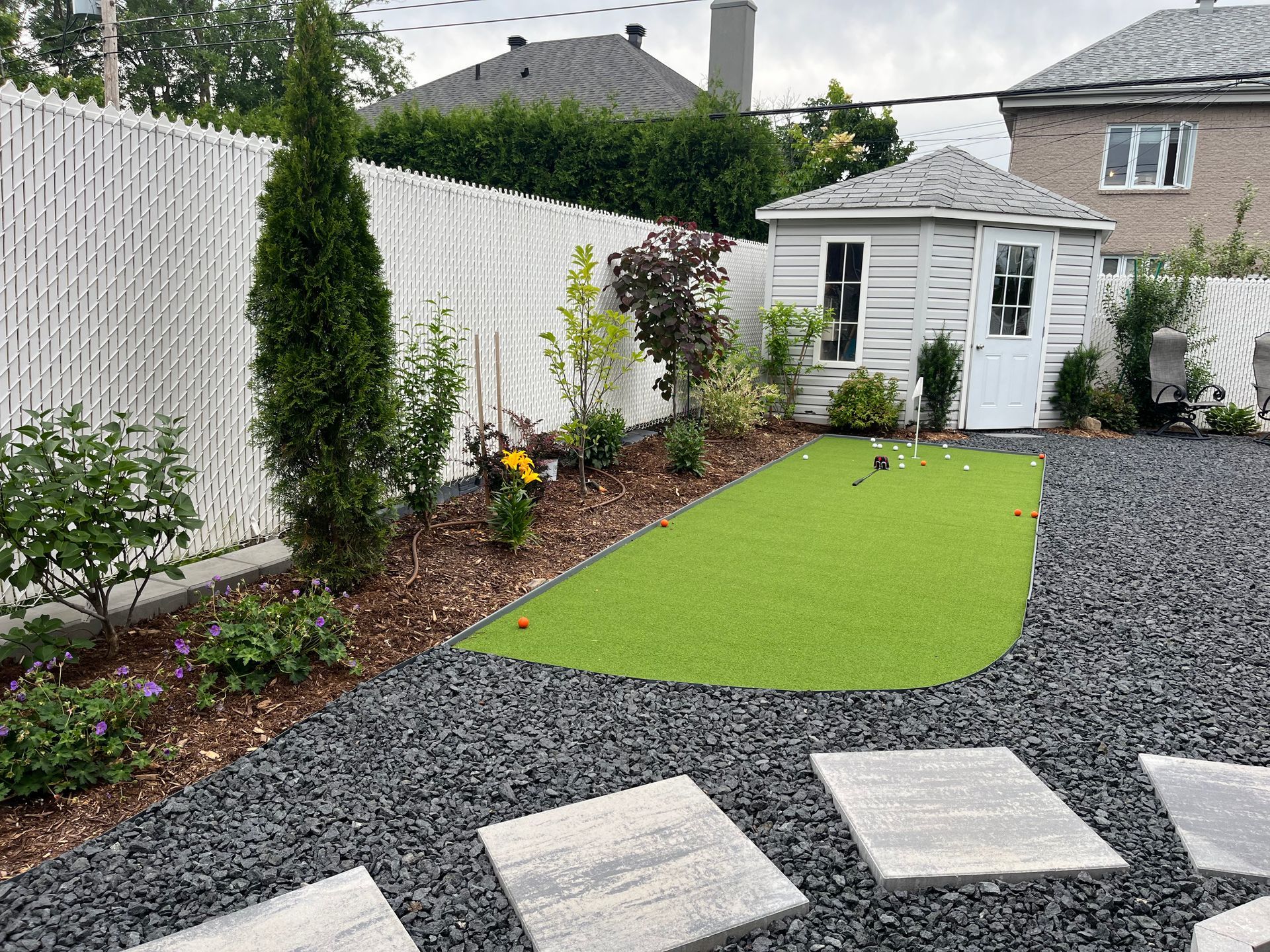 A backyard with a white fence and a small house in the background.