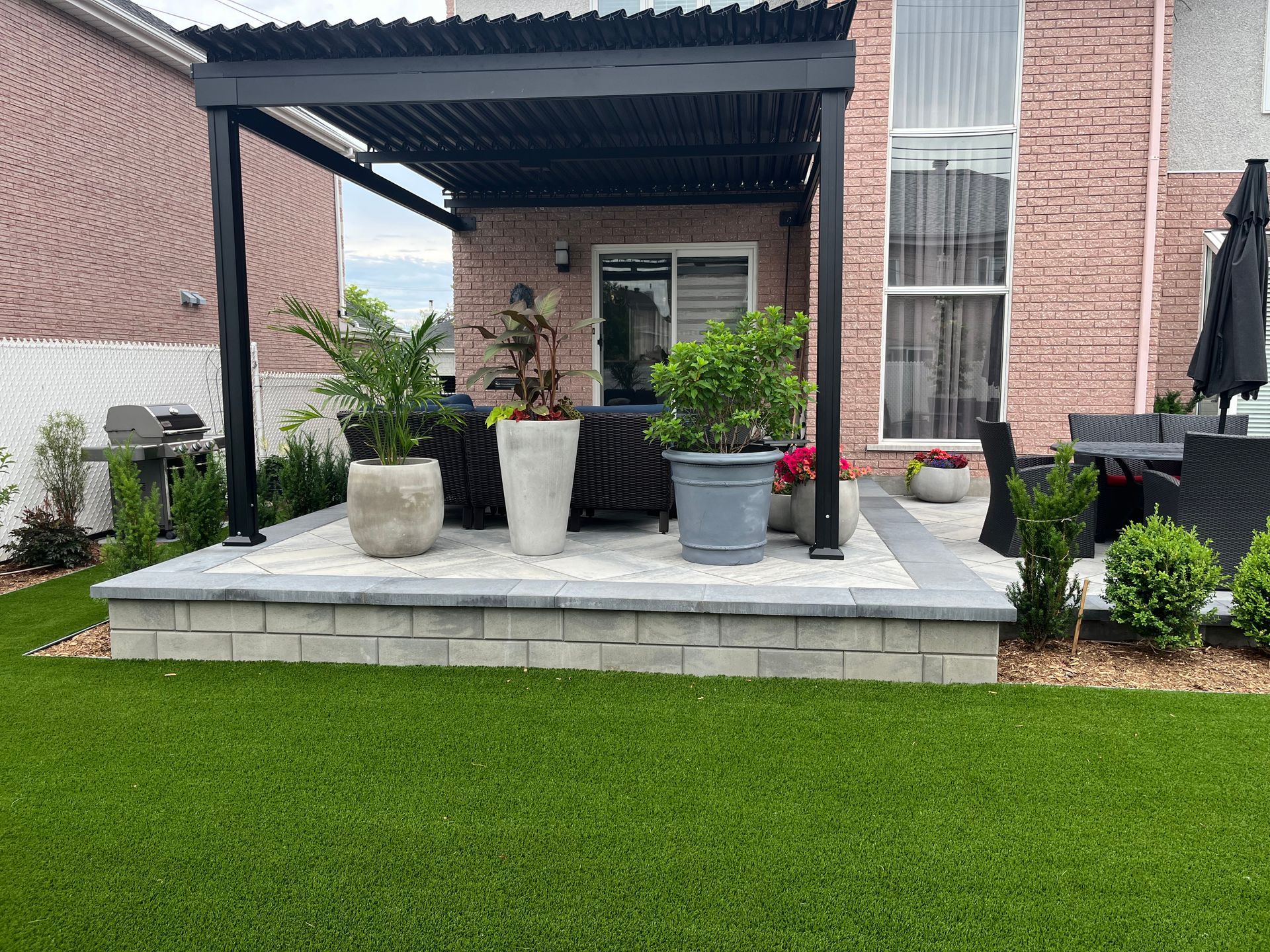 A patio with a pergola and potted plants in front of a brick house.