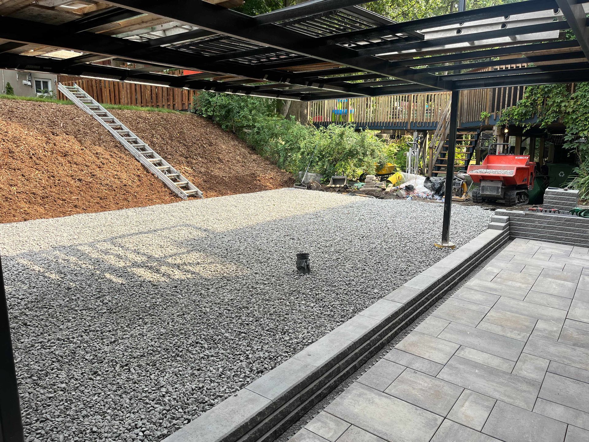 A gravel driveway with a patio and a ladder in the background.