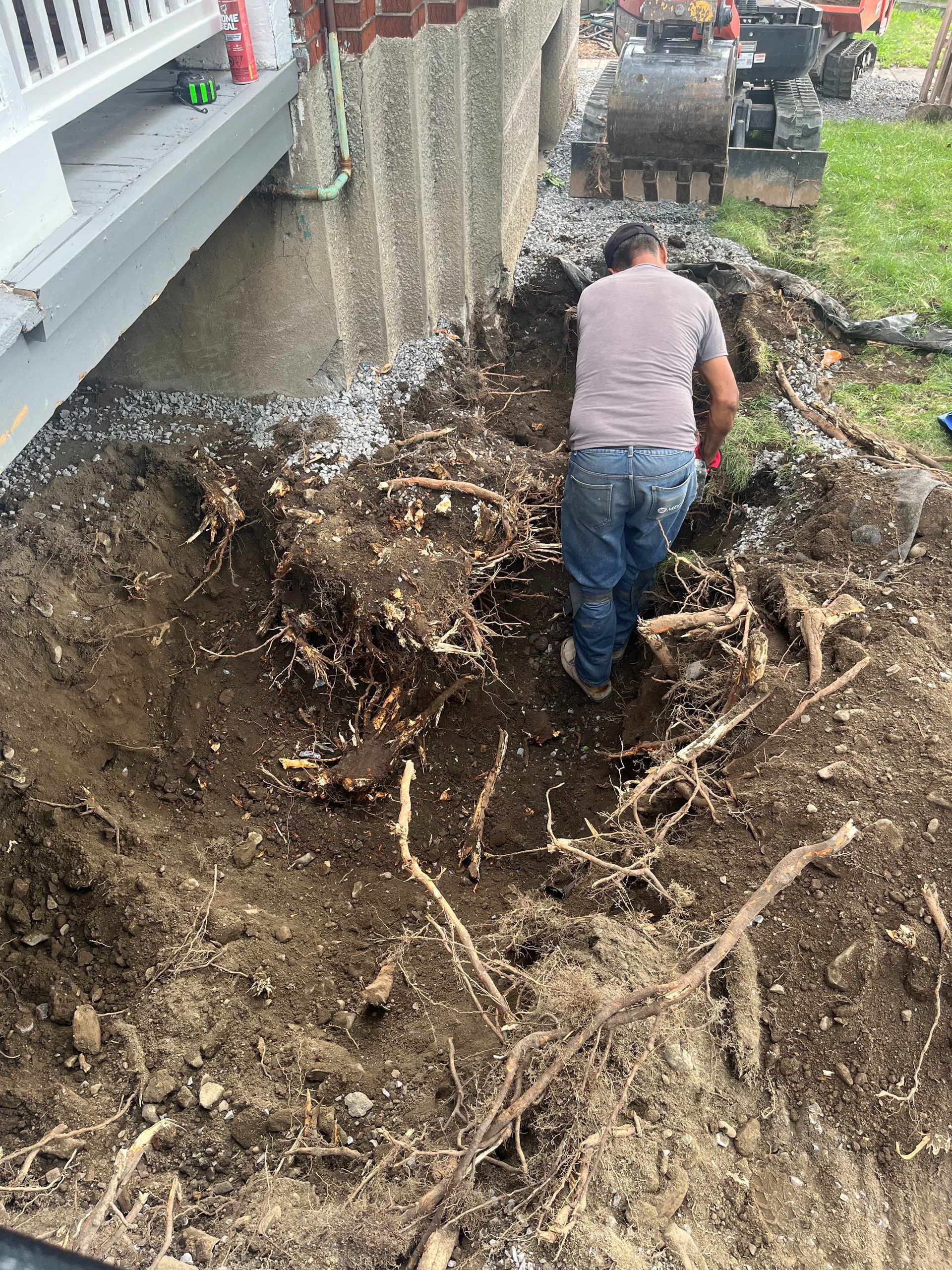 A man is digging a hole in the dirt in front of a house.