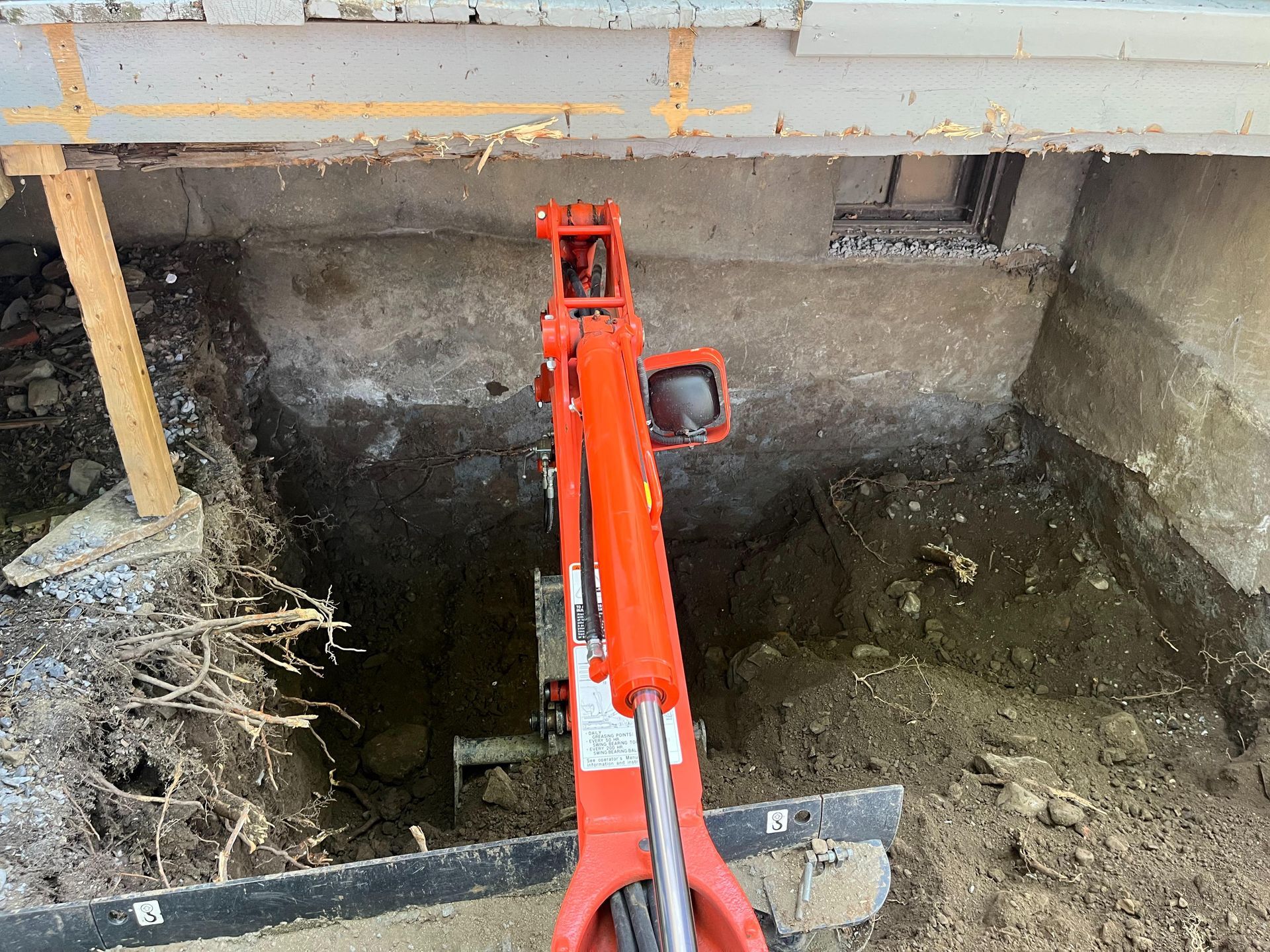 A red excavator is digging a hole in the ground.