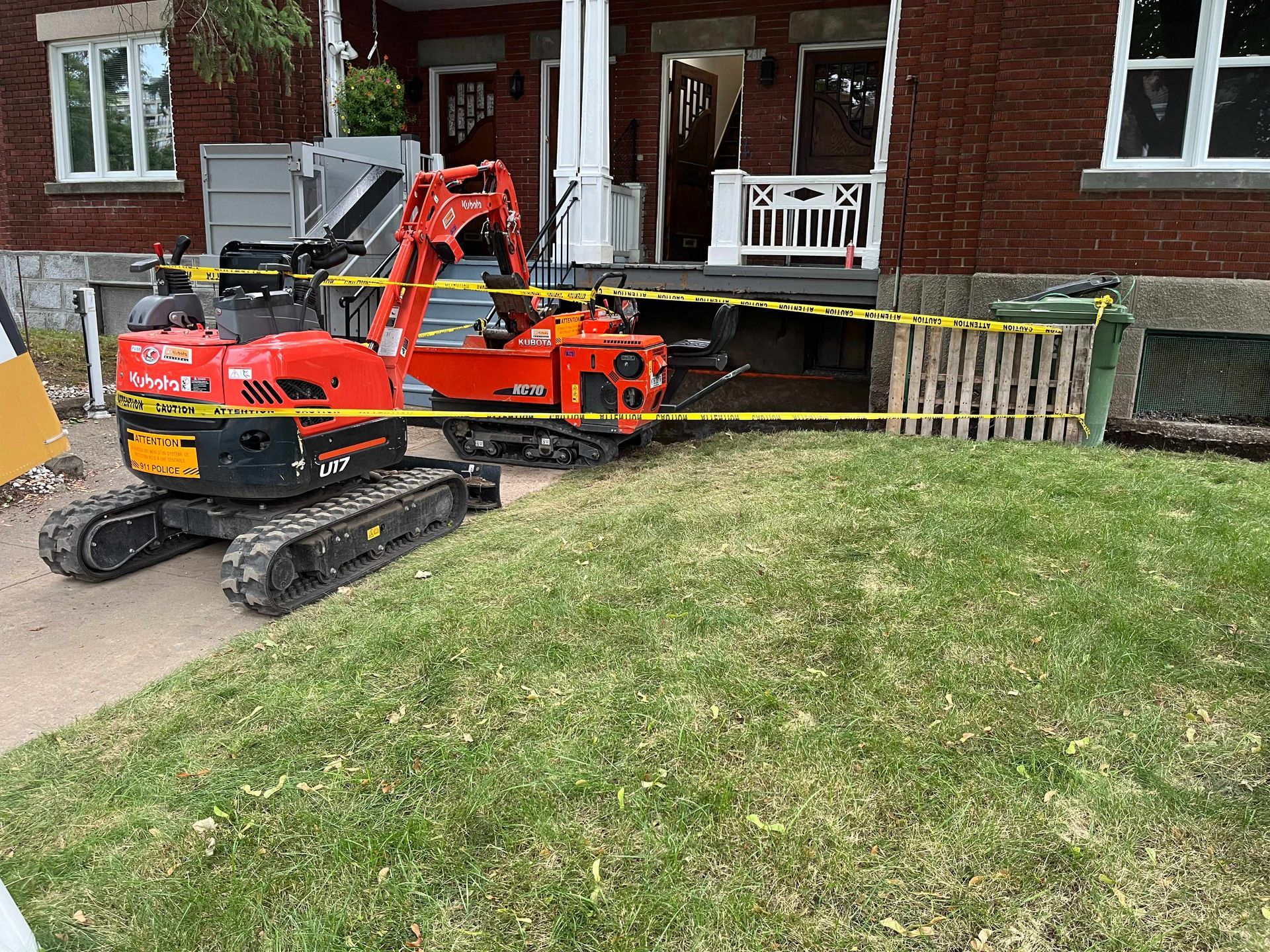 A small orange excavator is parked in front of a brick house.