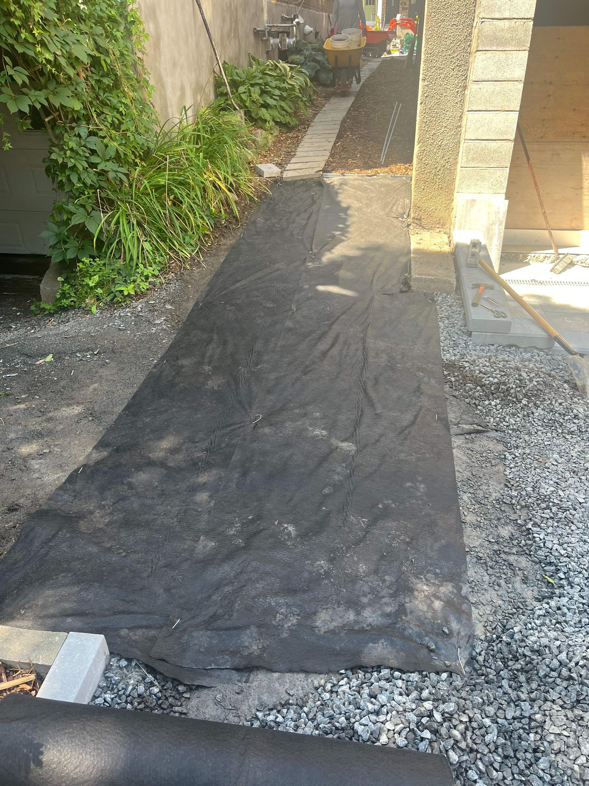 A black tarp is laying on the ground next to a gravel path.