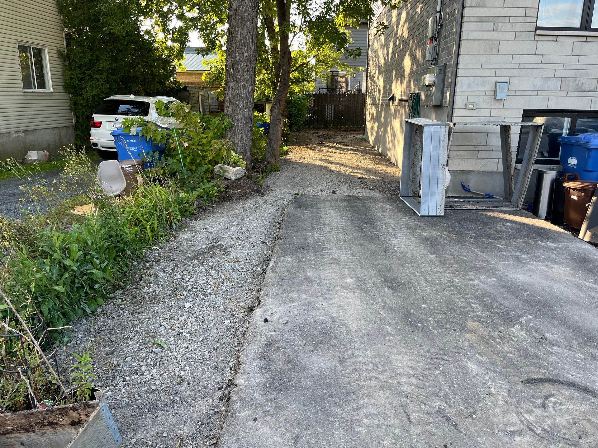 A driveway leading to a house with trash cans on the side of it.