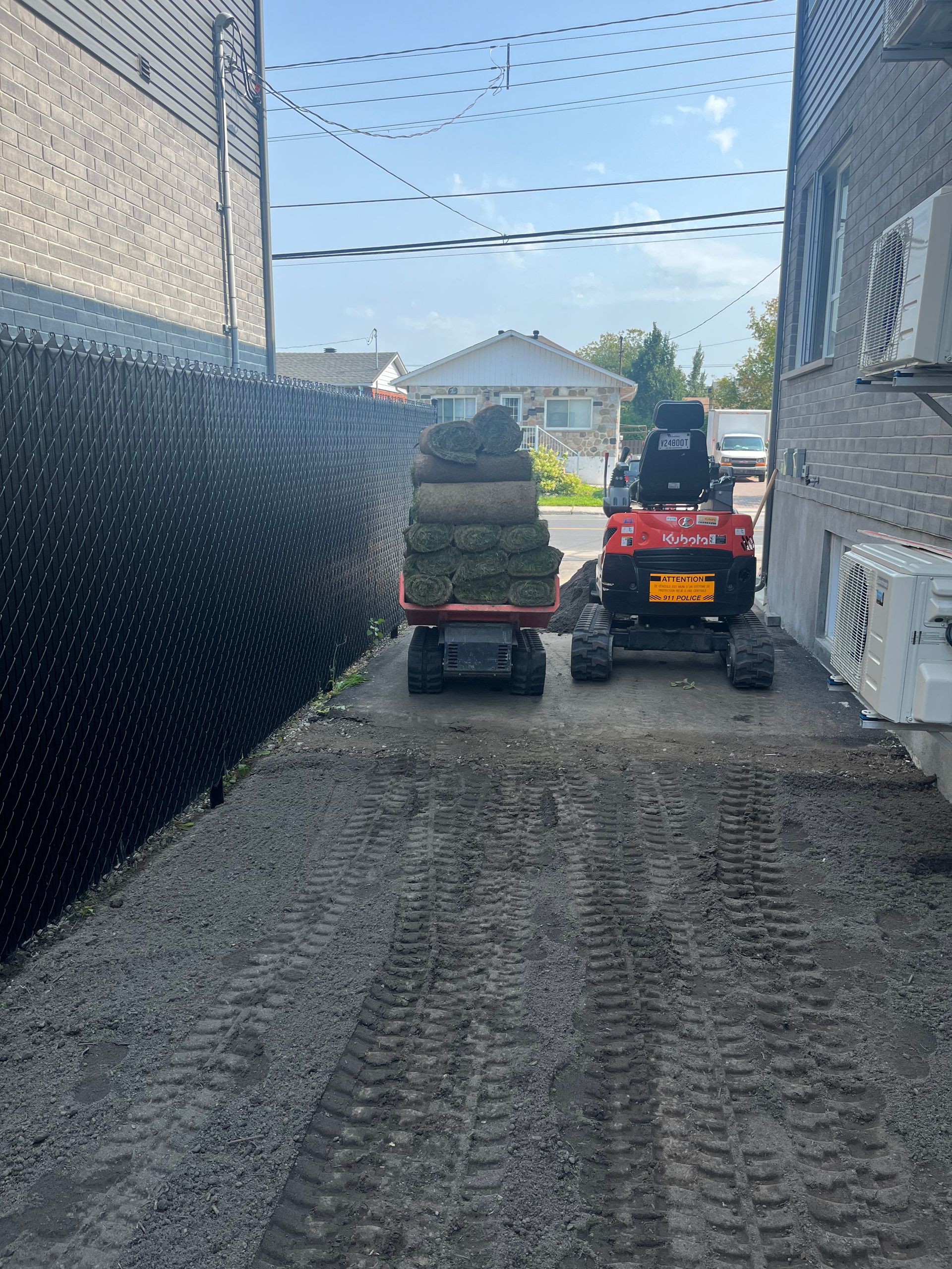 A small red tractor is carrying a trailer full of grass.
