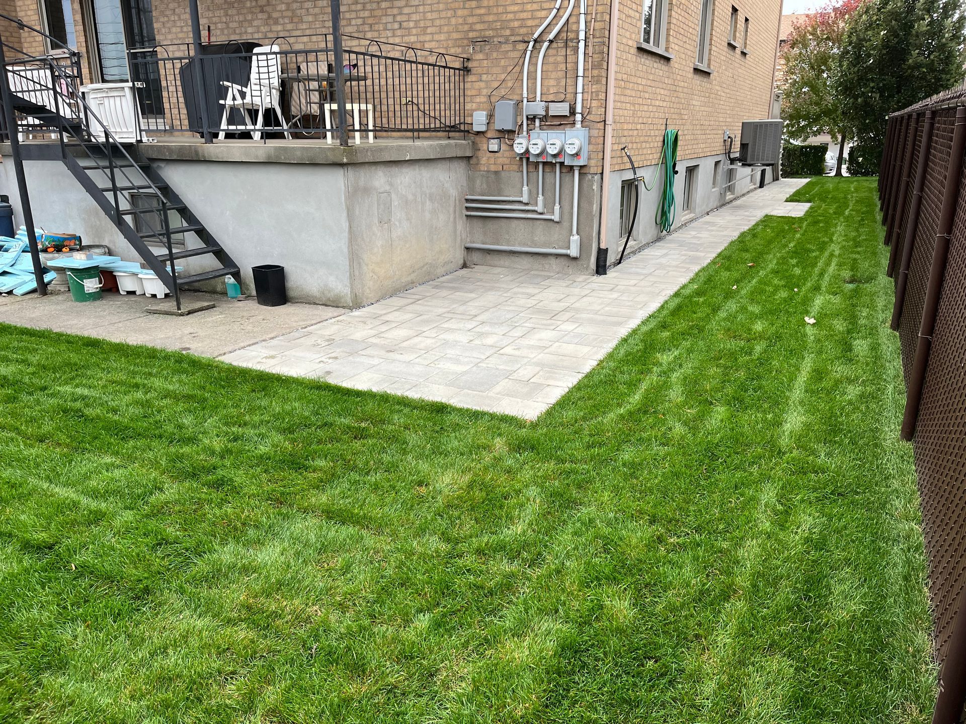 A lush green lawn is surrounded by a brick building and a fence.