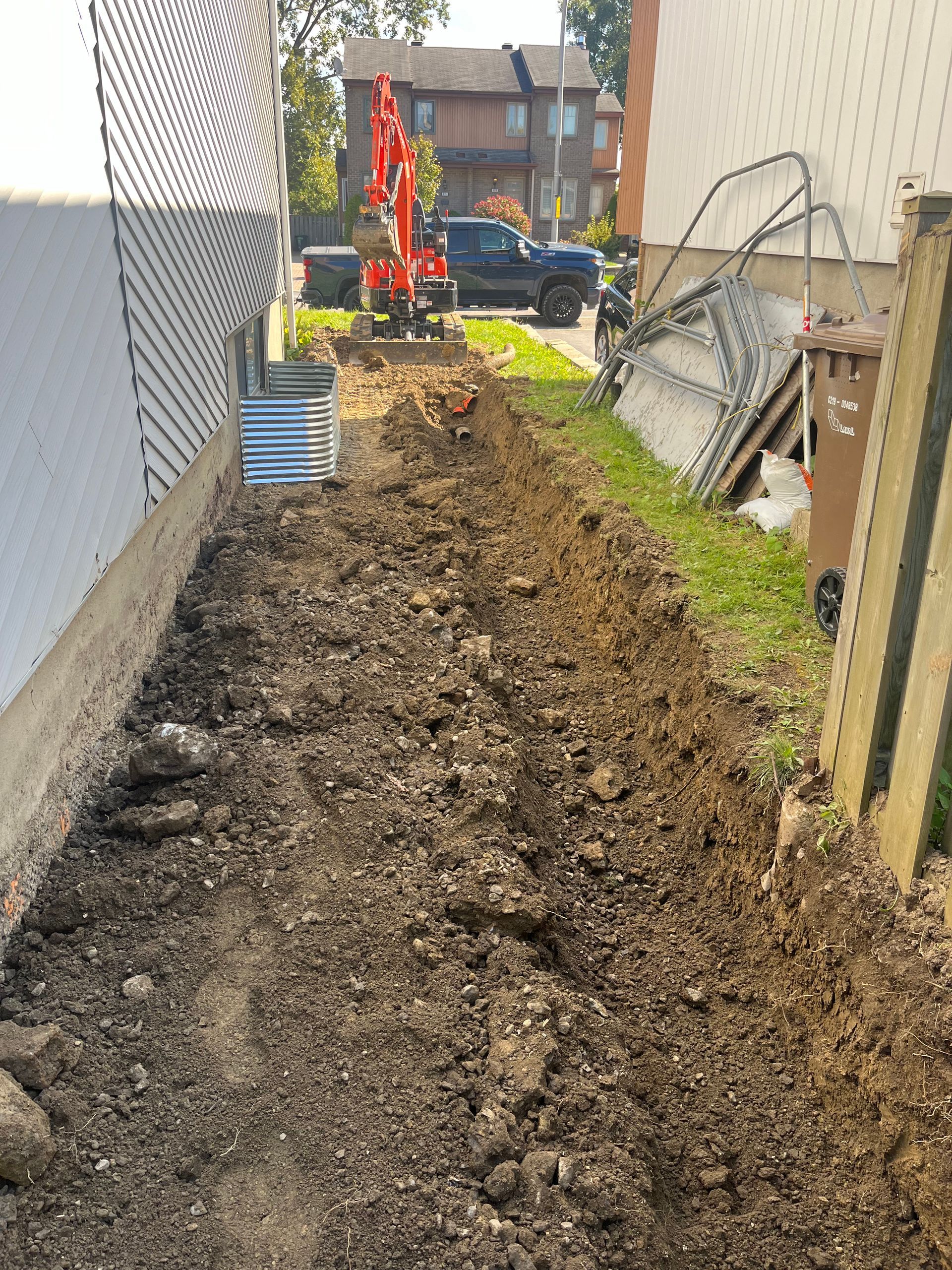 A red excavator is digging a hole in the dirt next to a building.