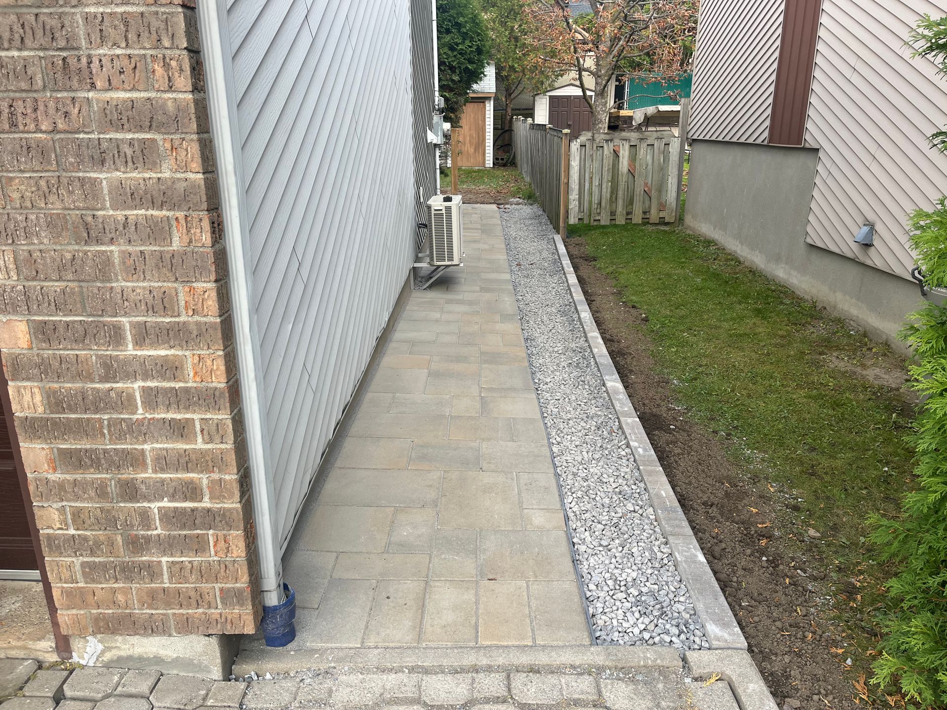 A sidewalk leading to a house with a brick wall and a fence.
