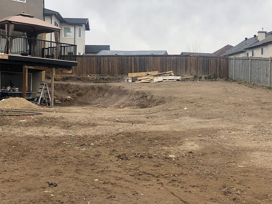 A large dirt field with a fence and a house in the background.