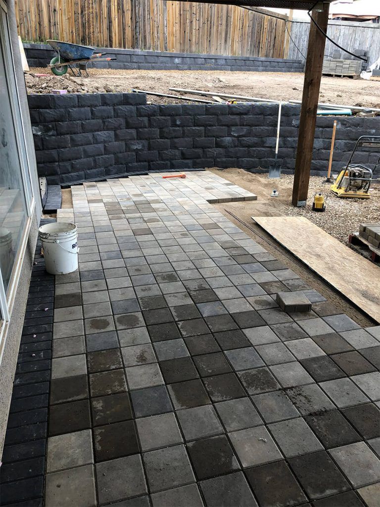 A brick patio is being built in a backyard.