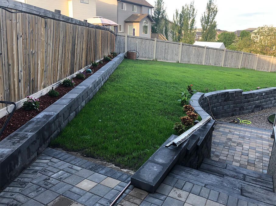 A backyard with a brick walkway and a wooden fence.